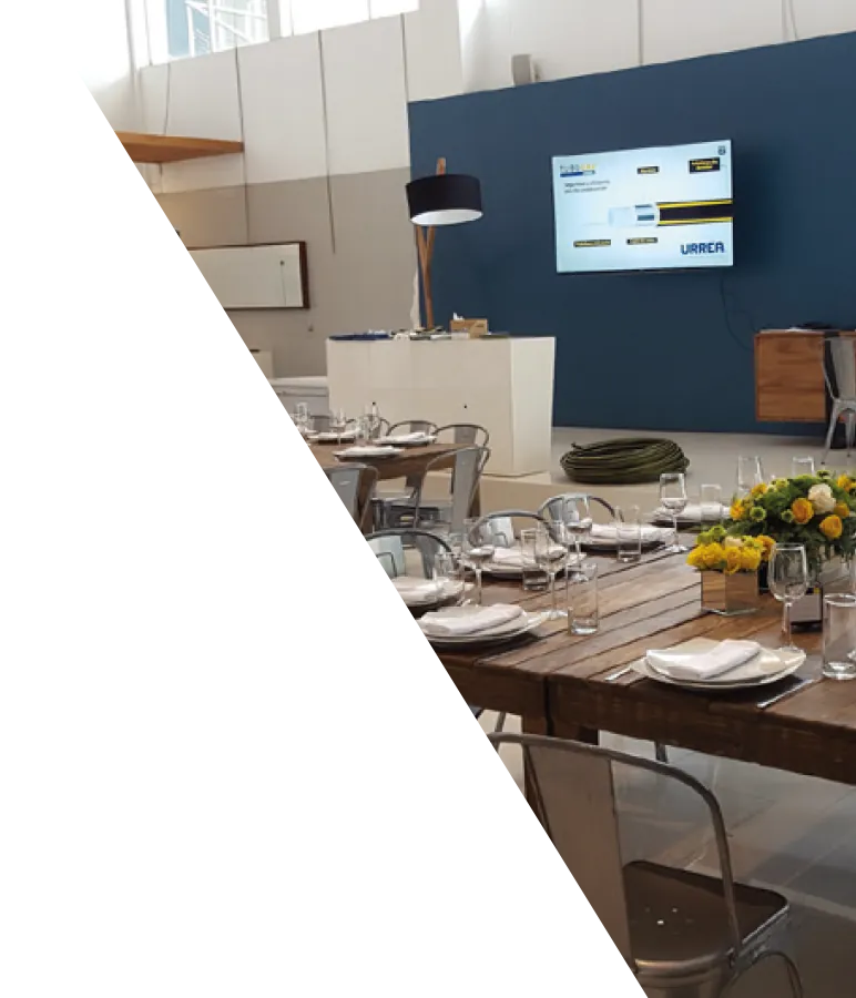 Montaje de evento corporativo con mesas decoradas y pantalla de marca